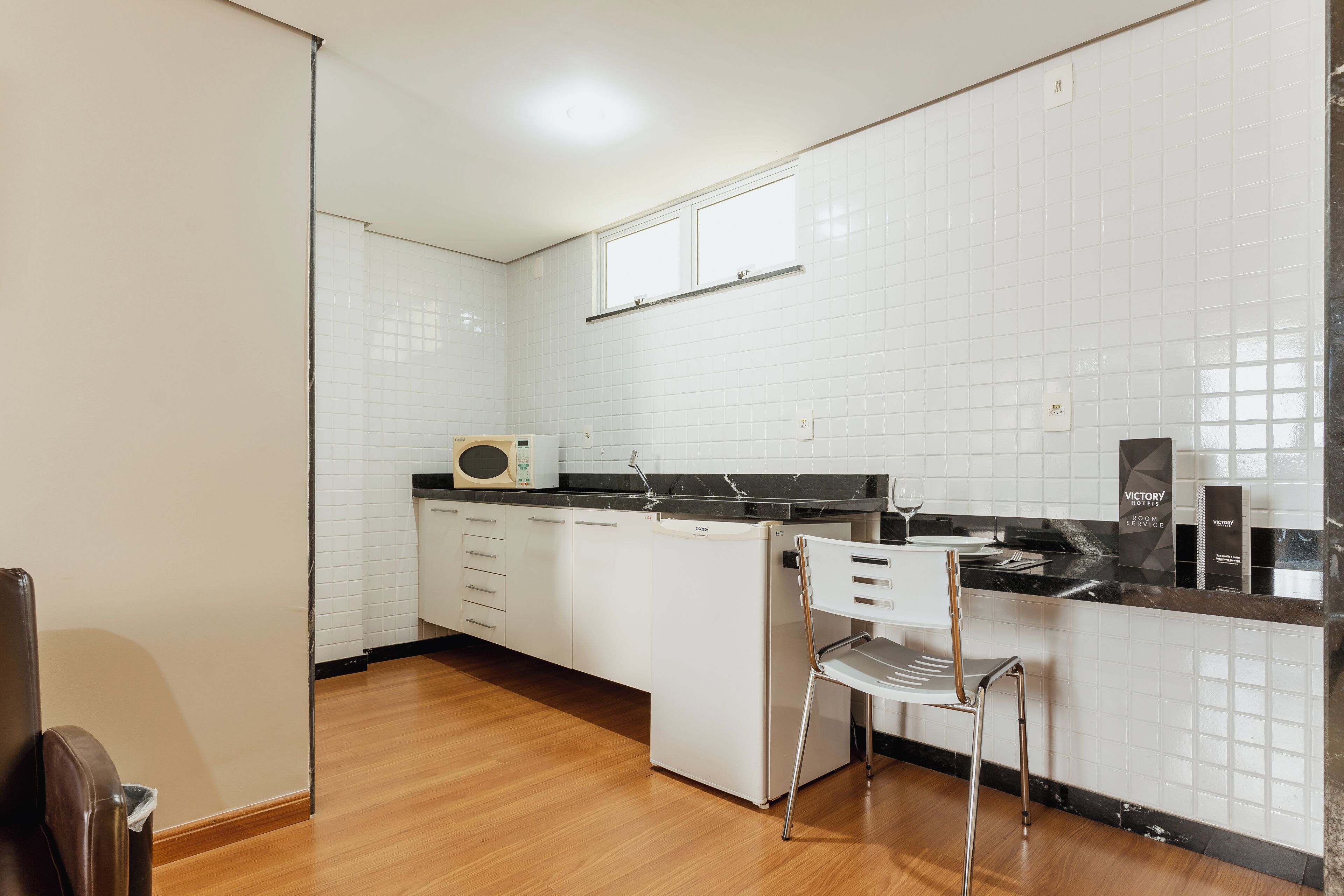 A kitchen with white cabinets, a black countertop, a microwave, and a chair.