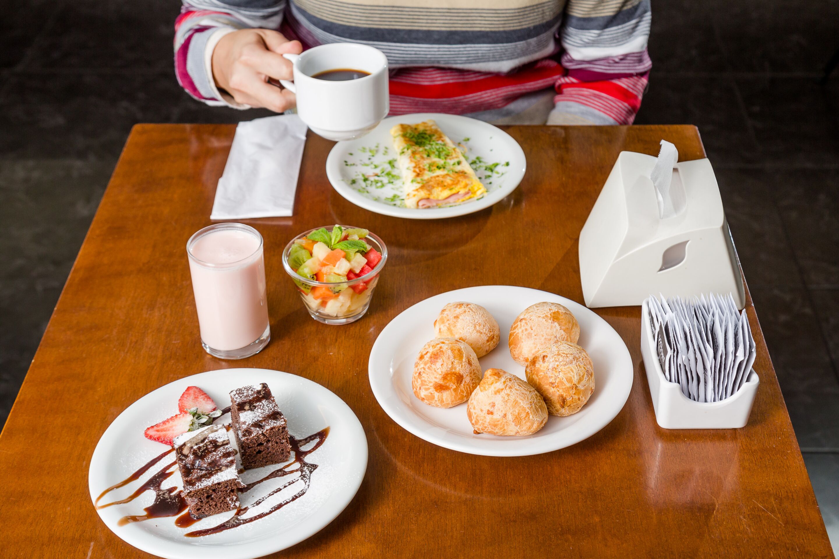 A table with a dessert plate, a plate of pastries, a glass of milk, a cup of coffee, and a small salad.