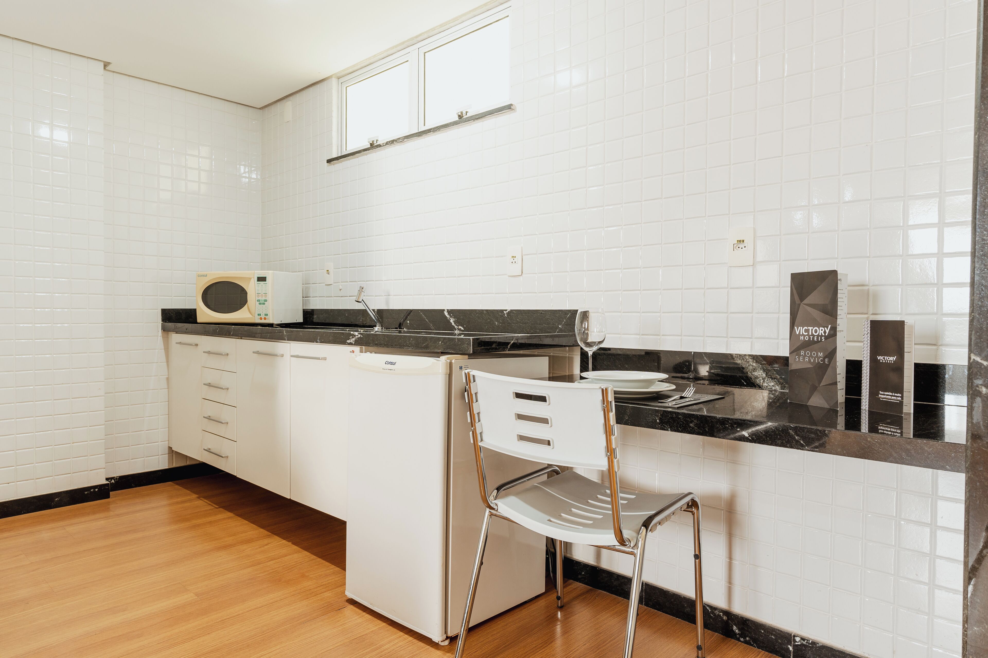 Una cocina con armarios blancos, microondas, lavabo y una silla.