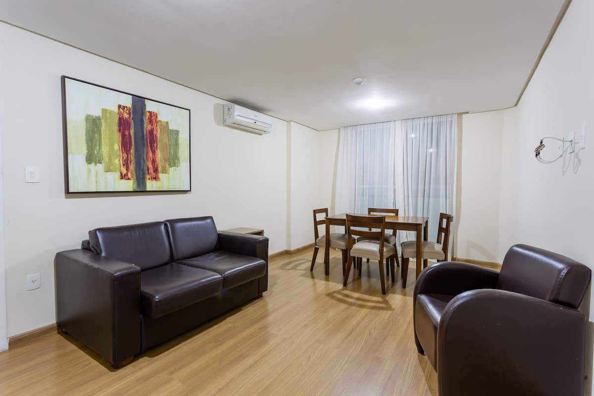 A modern living room with a leather sofa, a dining table with chairs, and a large abstract painting on the wall.