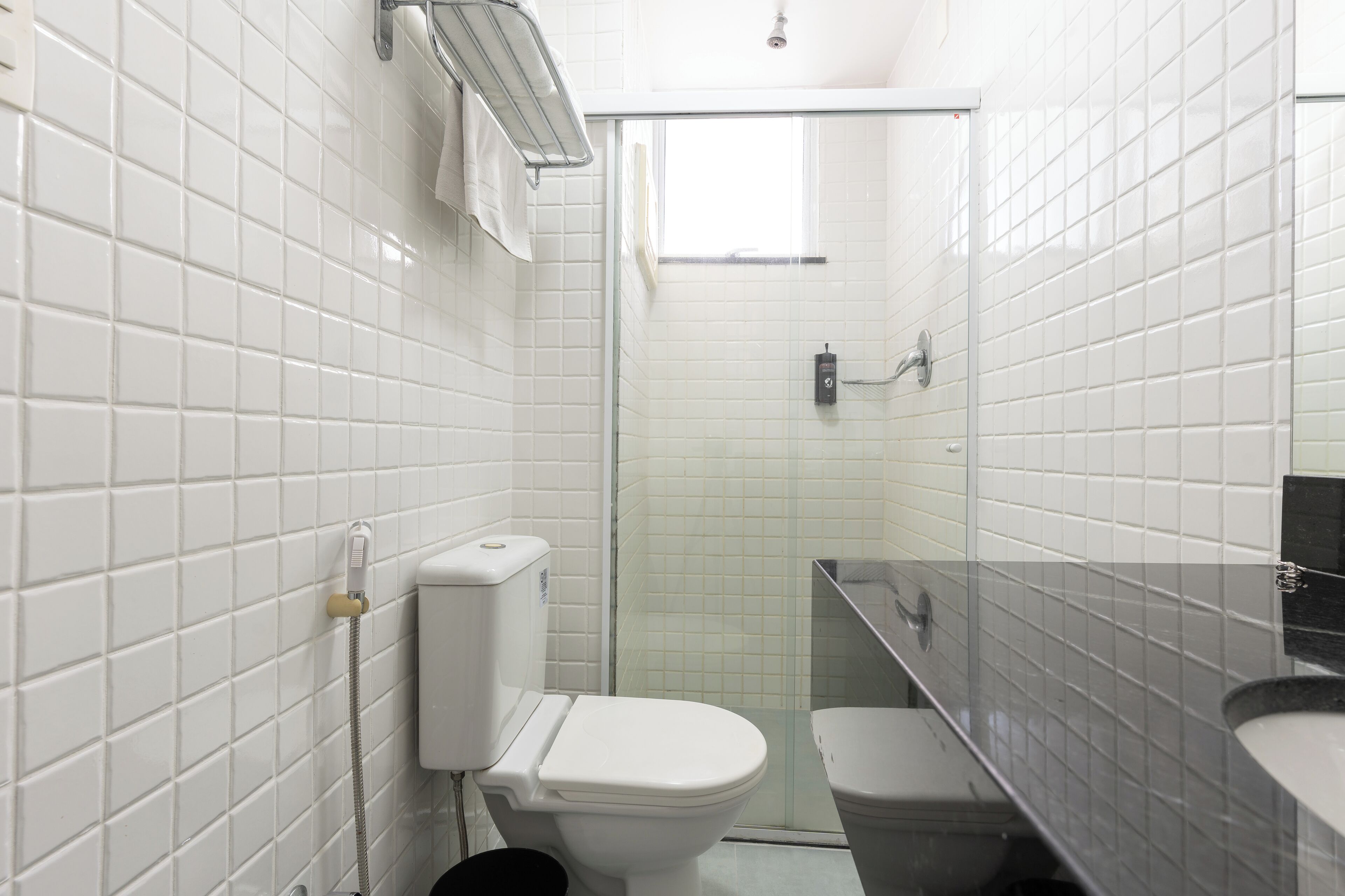 A bathroom with white tiled walls, a white toilet, a glass shower enclosure, and a black sink.