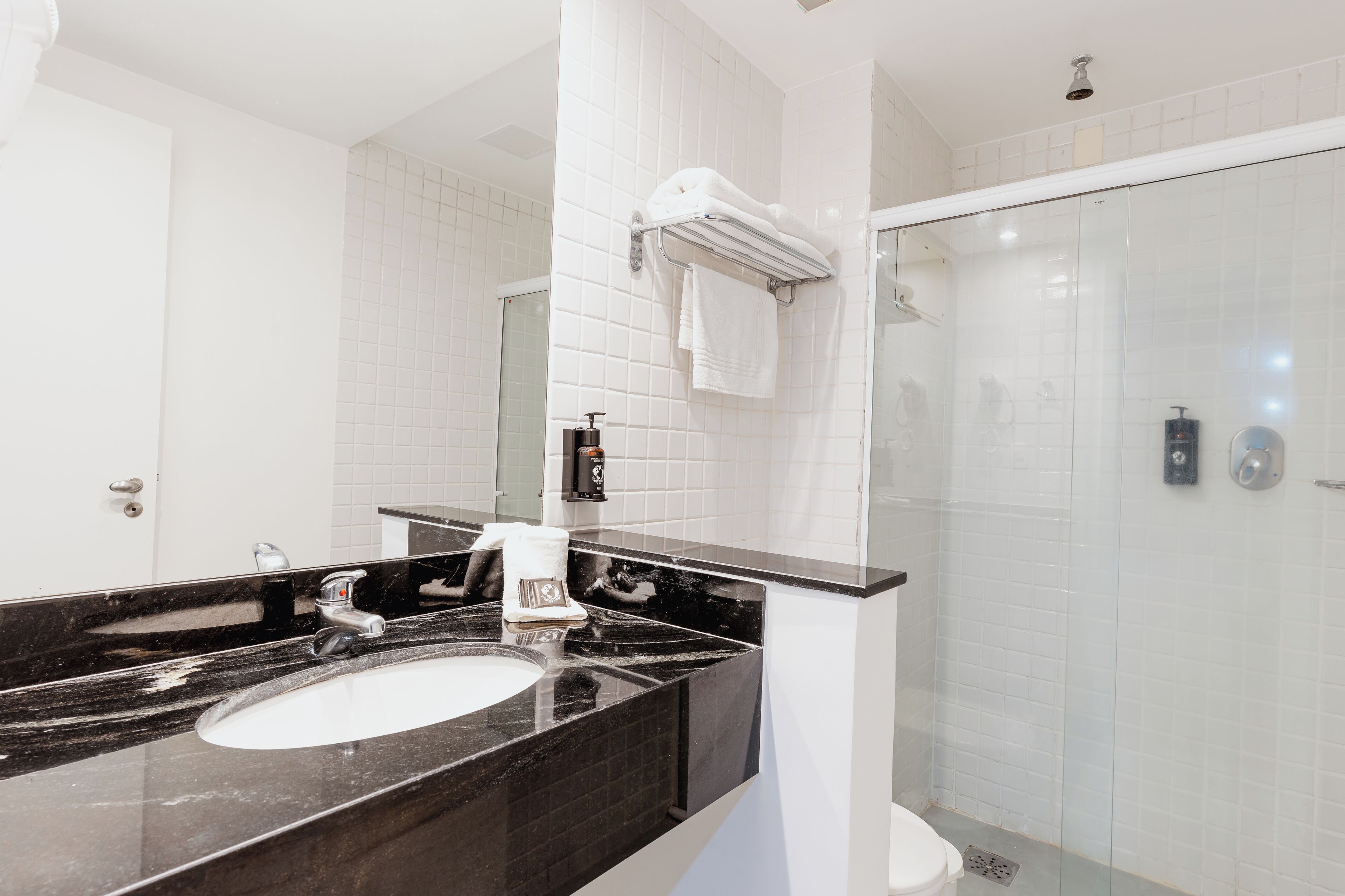 A modern bathroom with a black marble sink, white tiles, a glass shower enclosure, and a towel rack.
