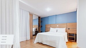 A modern hotel room with a wooden bed, a wardrobe, and a mirror. - Victory Suites (Juiz de Fora)
