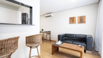 Un salon moderne avec un canapé en cuir noir, deux fauteuils en osier, une table basse en bois et un petit coin repas comprenant une table et des chaises.