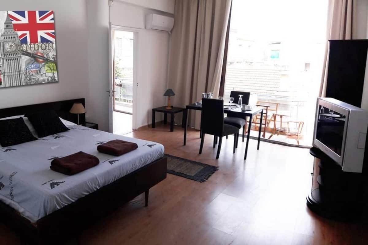 Habitación de hotel con cama, escritorio, silla, televisor y ventana con cortinas.