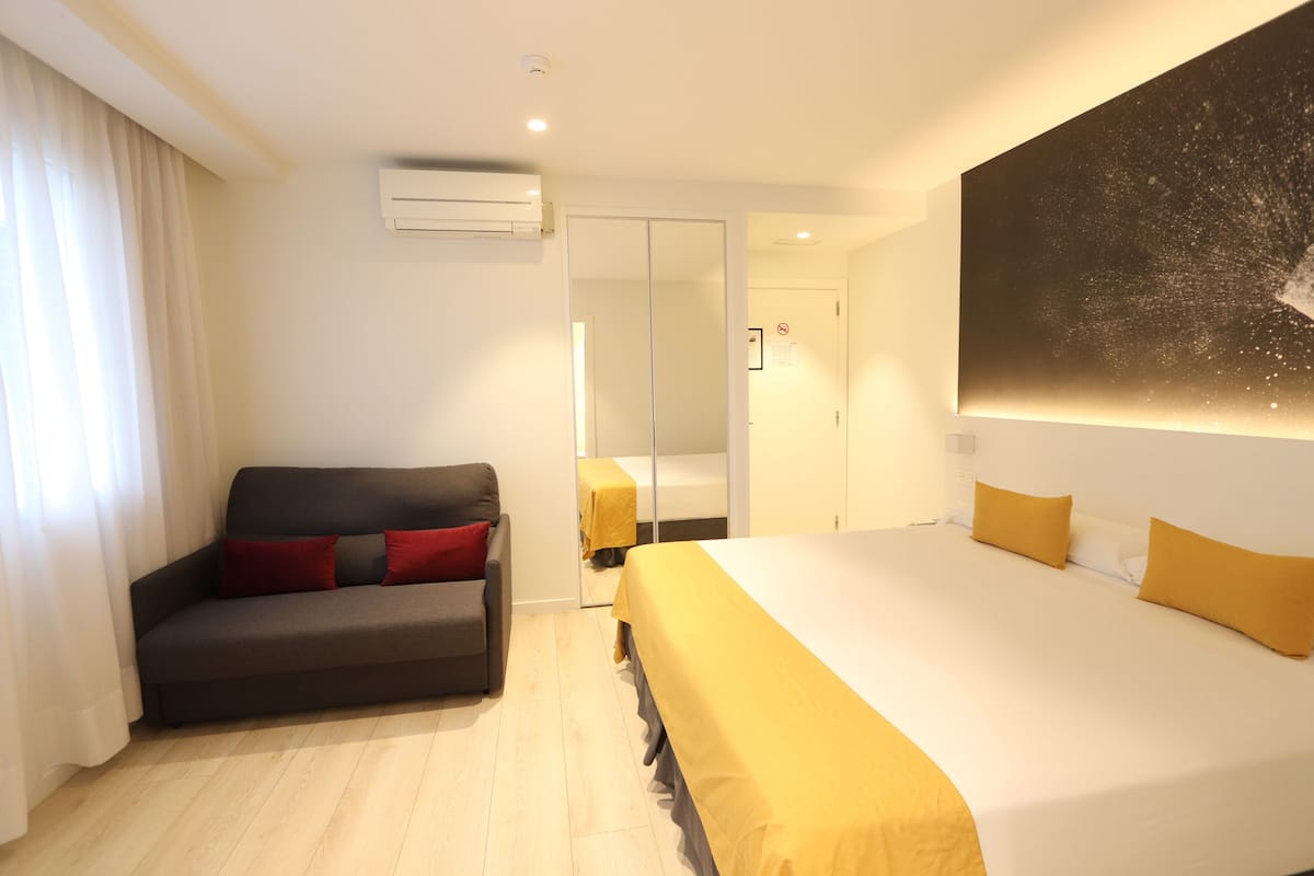 Quarto de hotel com uma cama, um sofá, um espelho e um quadro na parede.