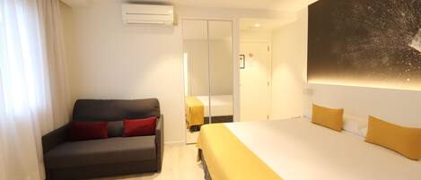Habitación de hotel con cama, sofá, espejo y un cuadro en la pared.