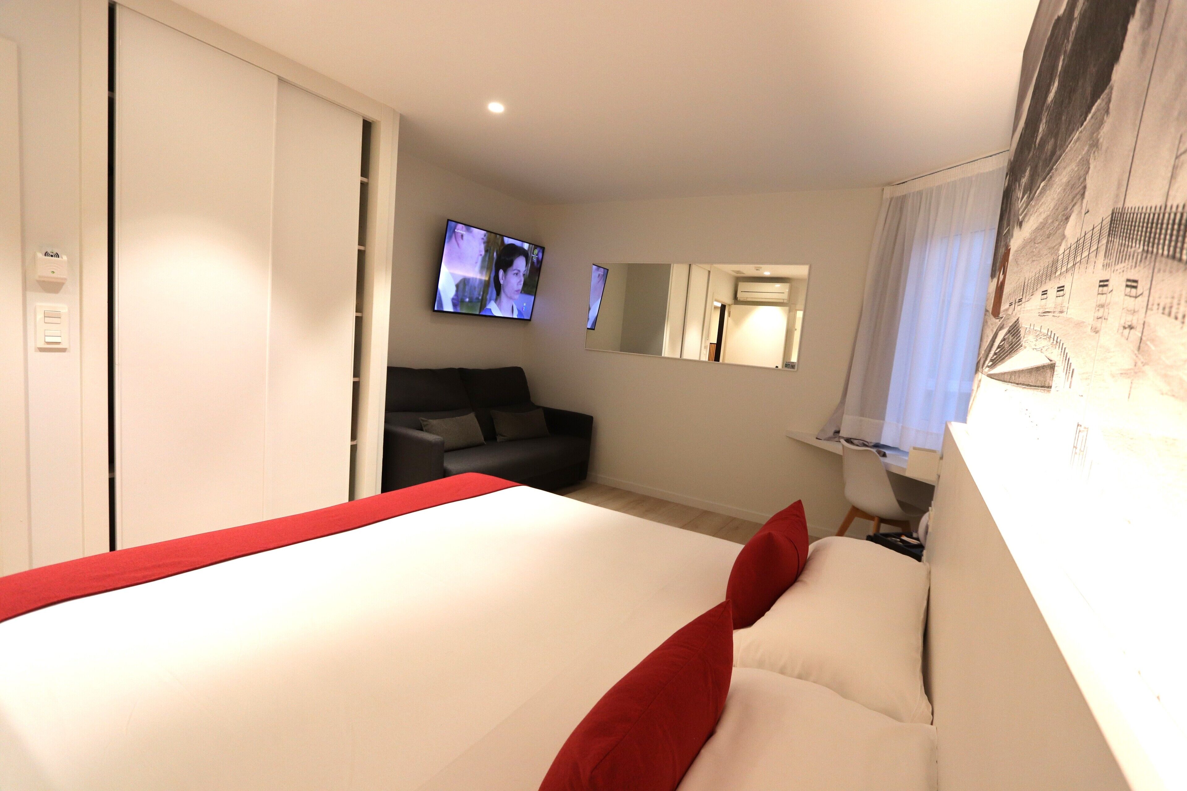 A hotel room with a bed, a TV, a sofa, a desk, and a mirror.