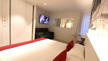 A hotel room with a bed, a TV, a sofa, a desk, and a mirror.
