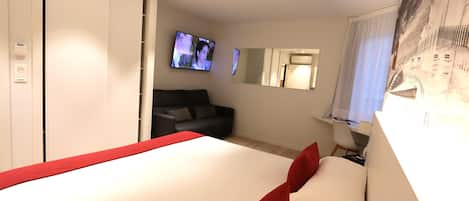 Ein Hotelzimmer mit Bett, Fernseher, Sofa, Schreibtisch und Spiegel.