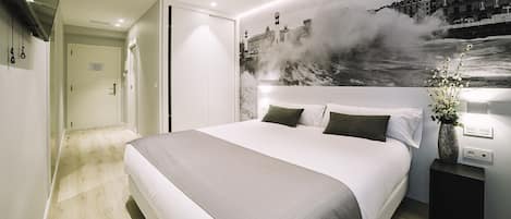 A modern hotel room with a large bed, a nightstand with a vase, and a wall mural of a cityscape.