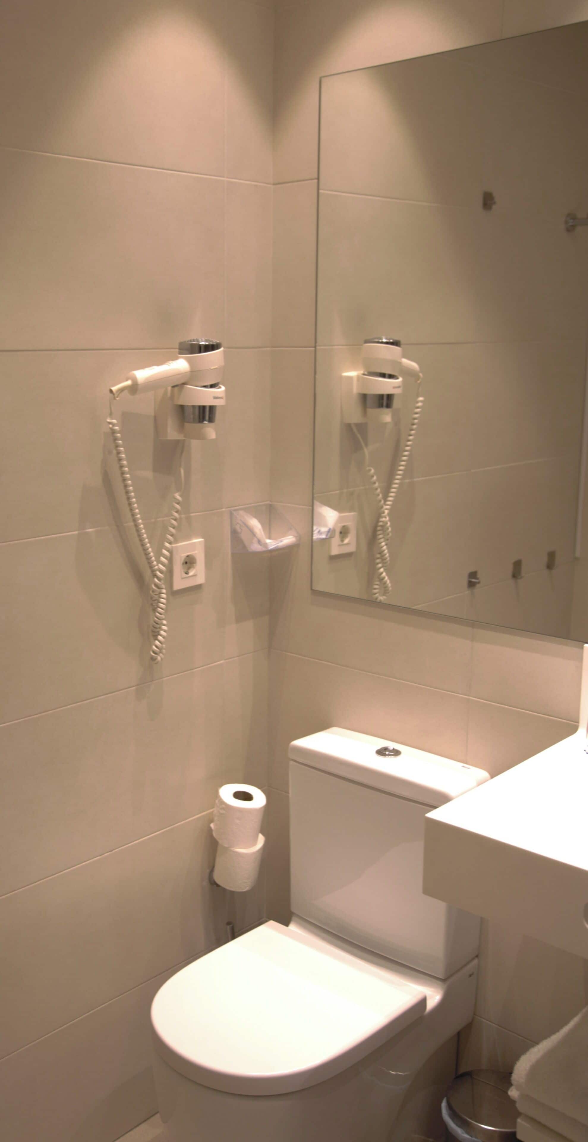 A bathroom with a toilet, a bidet, and a hairdryer mounted on the wall.