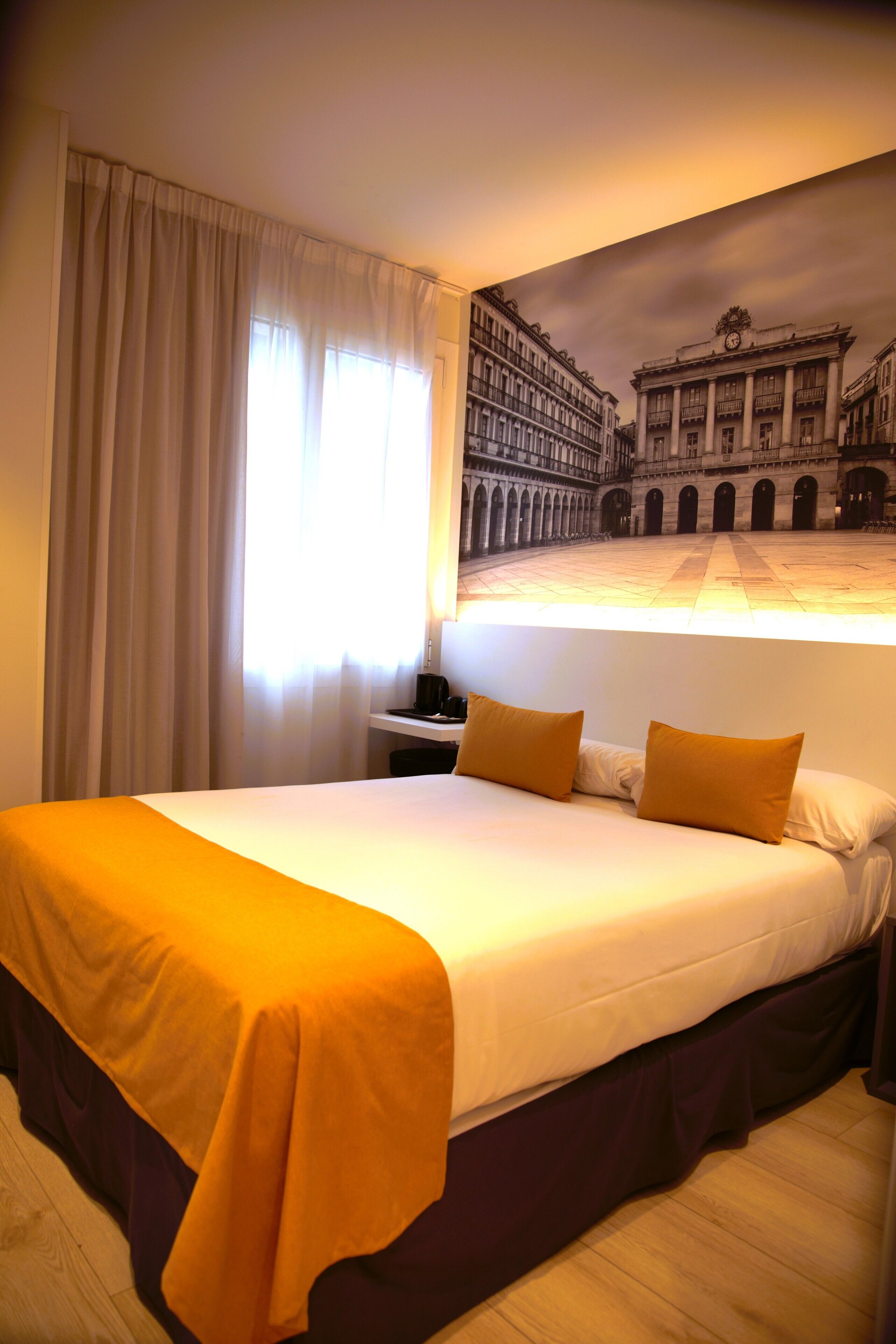 Habitación de hotel con una cama grande, una mesita de noche, una lámpara y vistas a un edificio histórico por la ventana.