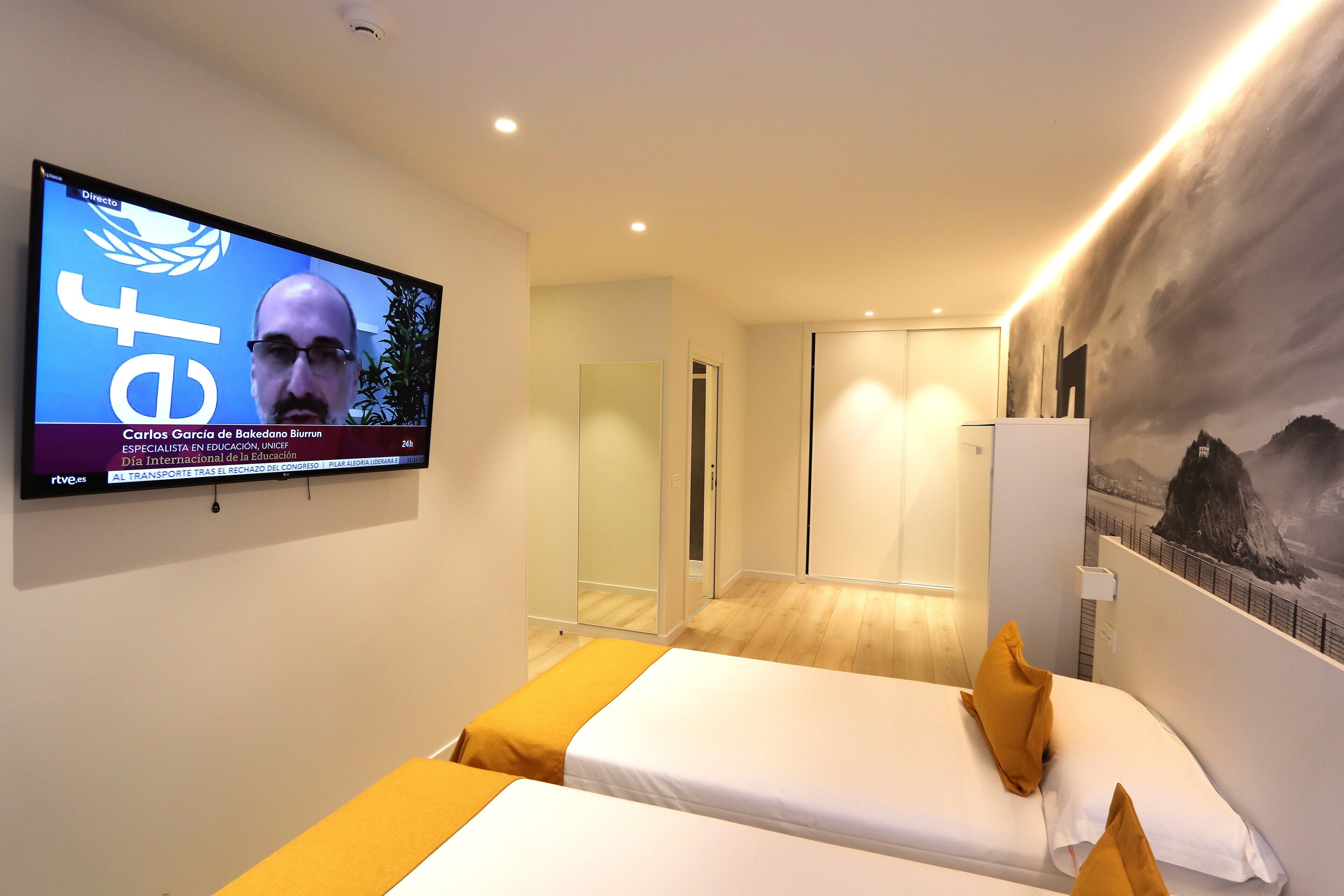 A hotel room with a bed, a TV mounted on the wall, and a mural on the wall.
