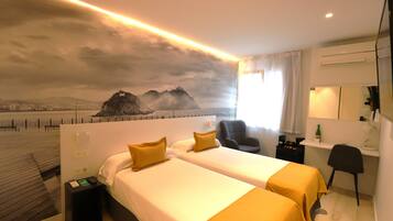 Une chambre d’hôtel avec deux lits, un bureau, une chaise et une vue sur un paysage urbain dominé par des montagnes.