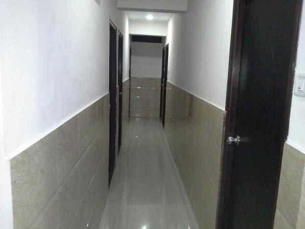 Un estrecho pasillo con baldosas, una puerta oscura a la derecha y una pared de color claro a la izquierda.