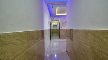 A hallway with marble walls and a reflective floor, leading to a room with a door at the end.