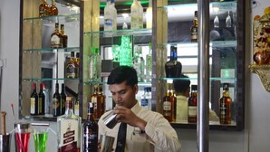 Un espace bar avec des étagères remplies de bouteilles d’alcool, un comptoir et un barman qui prépare un cocktail.