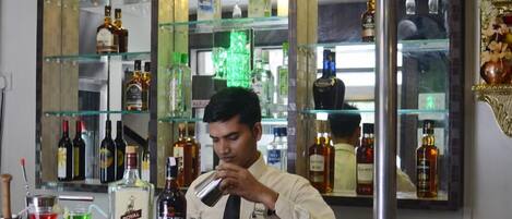 Zona de bar con estantes llenos de botellas de licor, barra y un barman preparando una bebida.