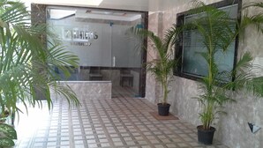 Un hall d’entrée avec un sol carrelé, des plantes en pot, un comptoir d’accueil et une enseigne indiquant « VIBHAW ».
