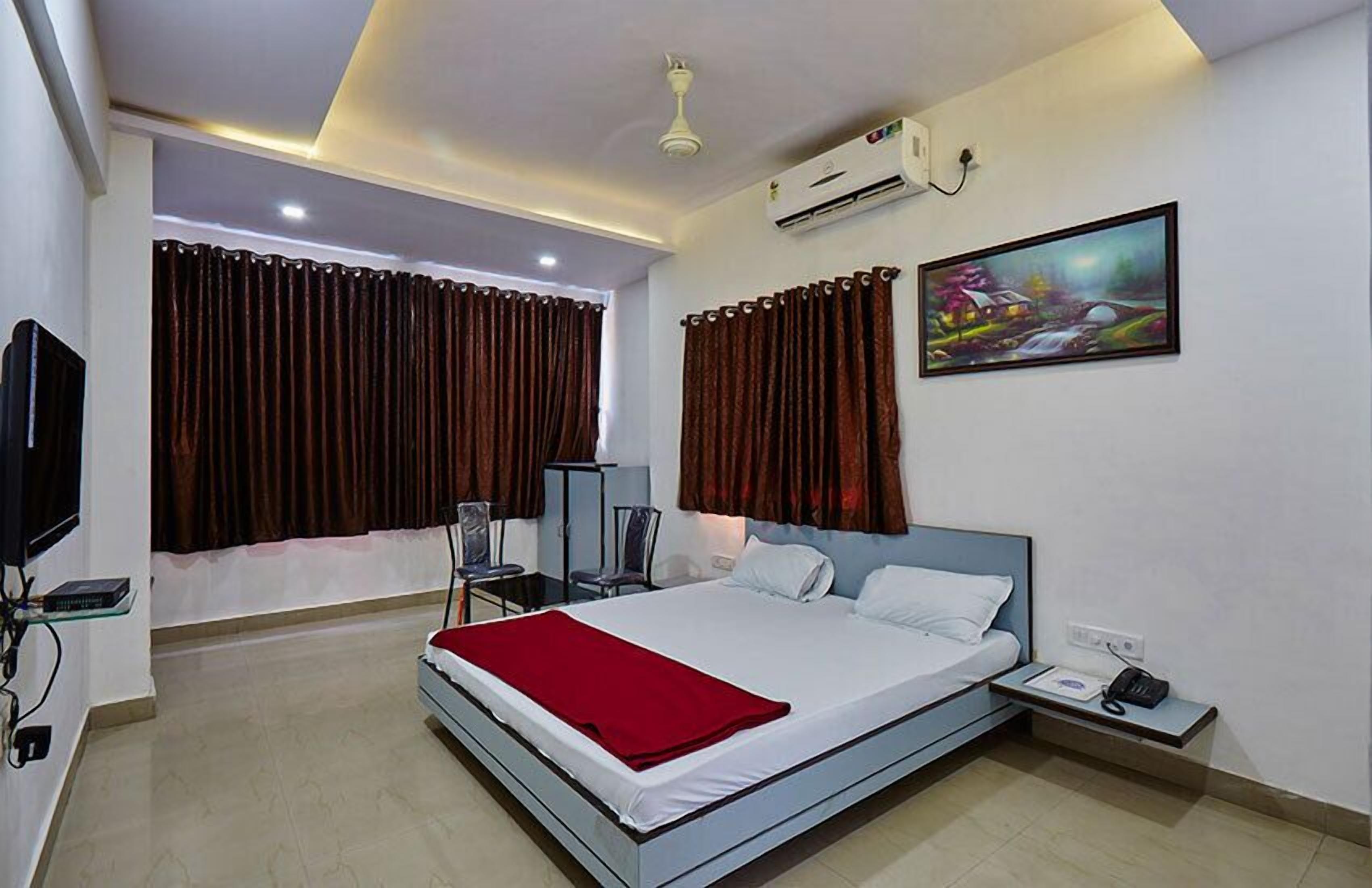 A modern hotel room with a large bed, a bedside table, a TV, and an air conditioning unit.