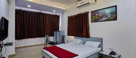 A modern hotel room with a large bed, a bedside table, a TV, and an air conditioning unit.