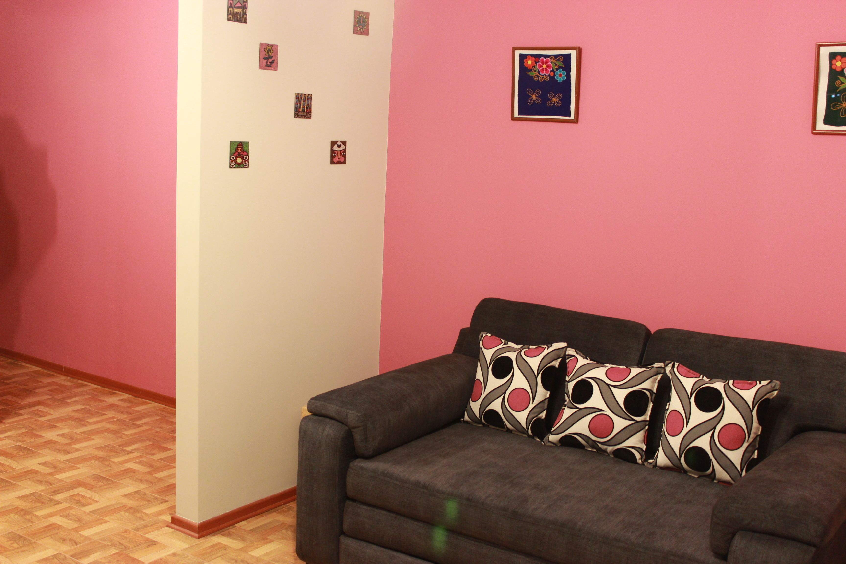 A living room with a brown sofa, two patterned pillows, and a pink wall with several small framed pictures.