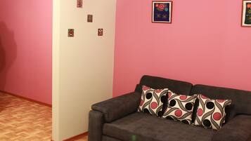 A living room with a brown sofa, two patterned pillows, and a pink wall with several small framed pictures.