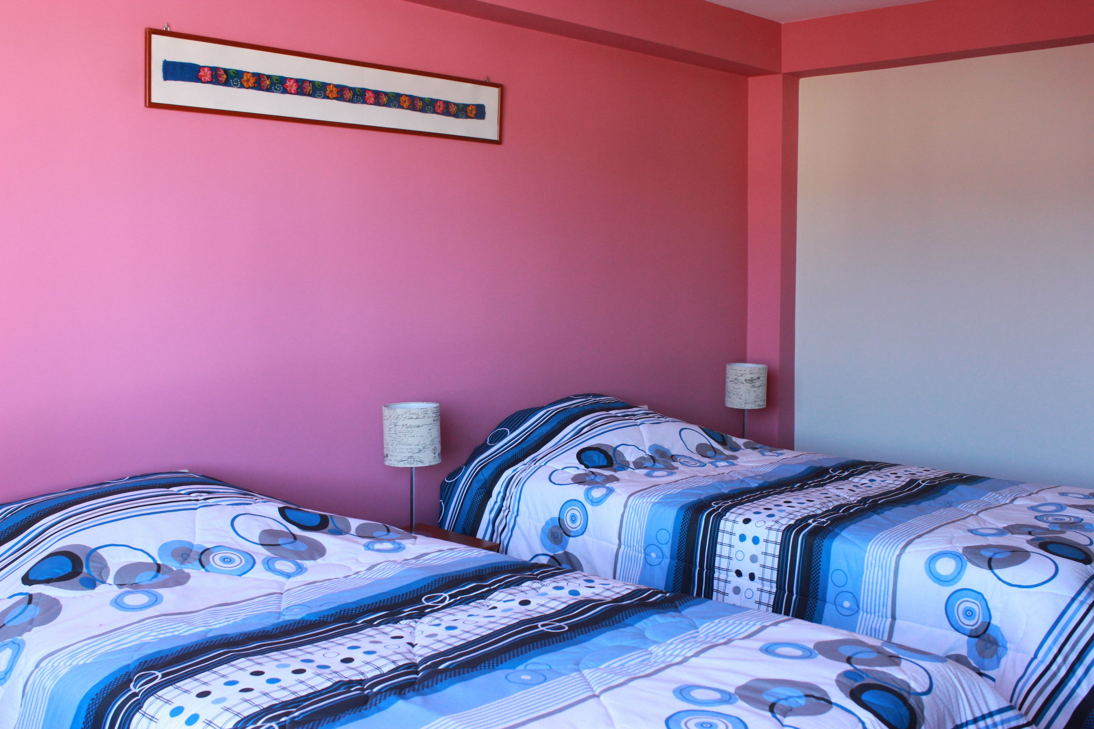 Un dormitorio con dos camas, paredes rosas y una obra enmarcada sobre las camas.