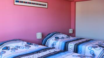Un dormitorio con dos camas, paredes rosas y una obra enmarcada sobre las camas.