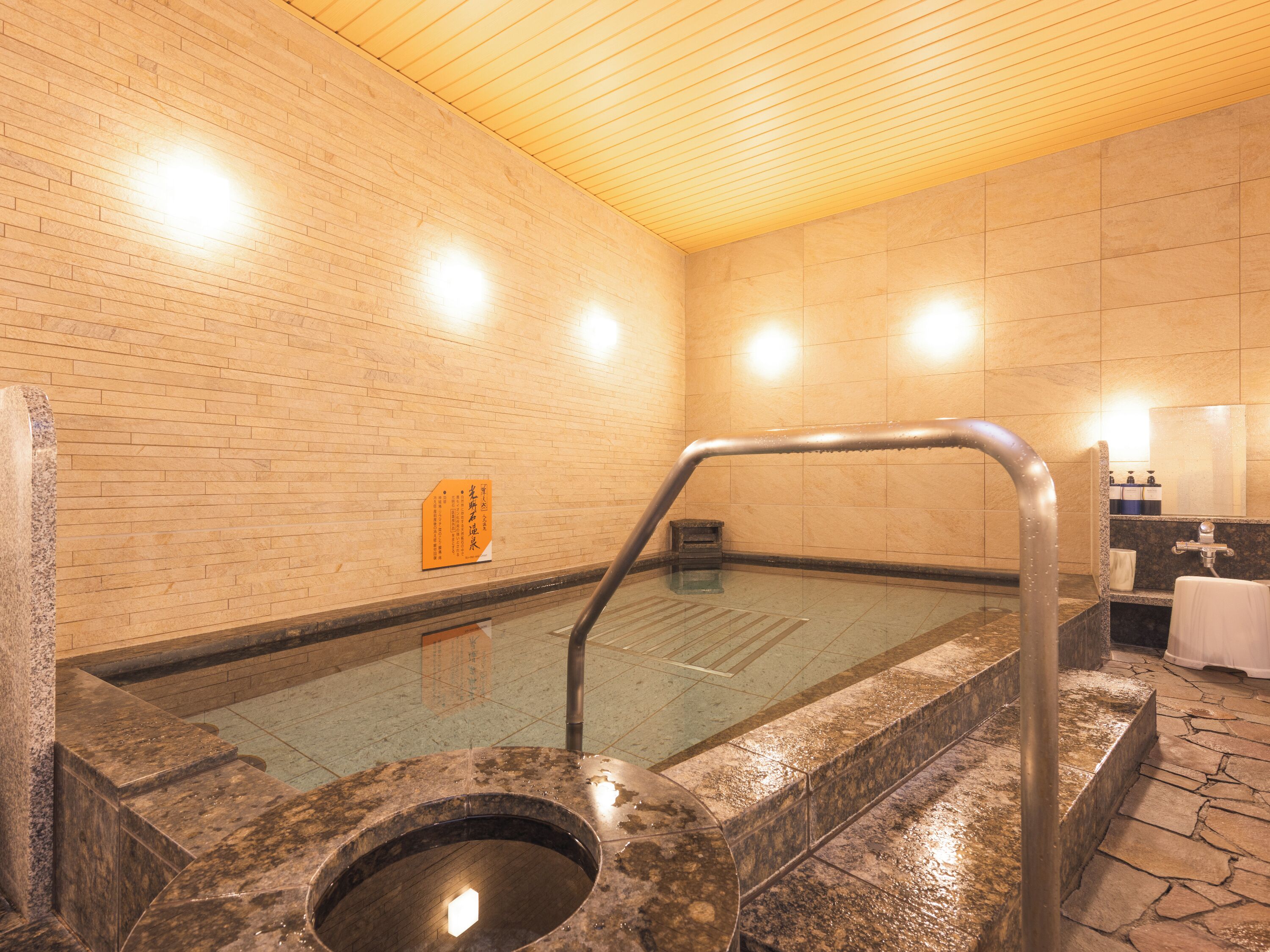 A hot spring bath area with a wooden ceiling, tiled walls, and a stone floor.