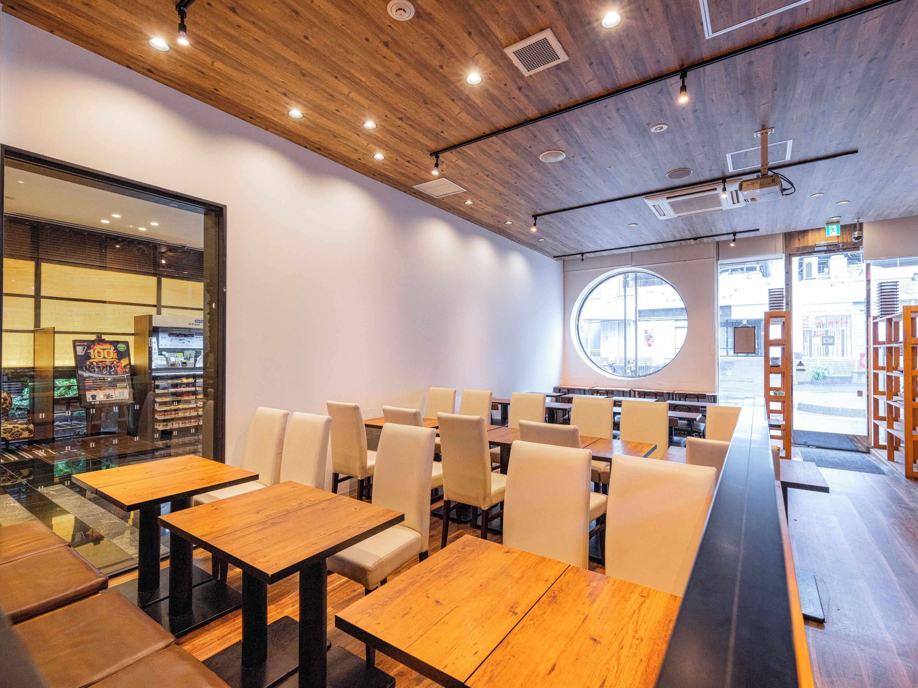 L’intérieur d’un restaurant moderne, avec des tables et des chaises en bois, une grande fenêtre ronde et une vue sur la rue.
