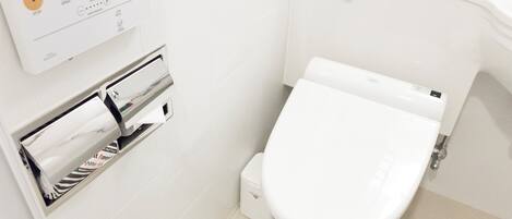 A modern bathroom with a toilet, a paper towel dispenser, and a hand dryer.