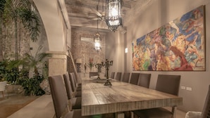 A dining area with a long wooden table, cushioned chairs, and a large mural on the wall.