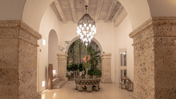A spacious lobby with a high ceiling, a central chandelier, and a seating area with a table and chairs.