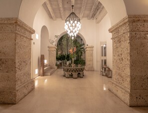 A spacious lobby with a high ceiling, a central chandelier, and a seating area with a table and chairs. - Hotel Noi 1860 Cartagena (Cartagena)