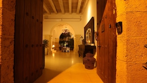 A hallway with wooden doors and a tiled floor leading to a room with a chandelier.