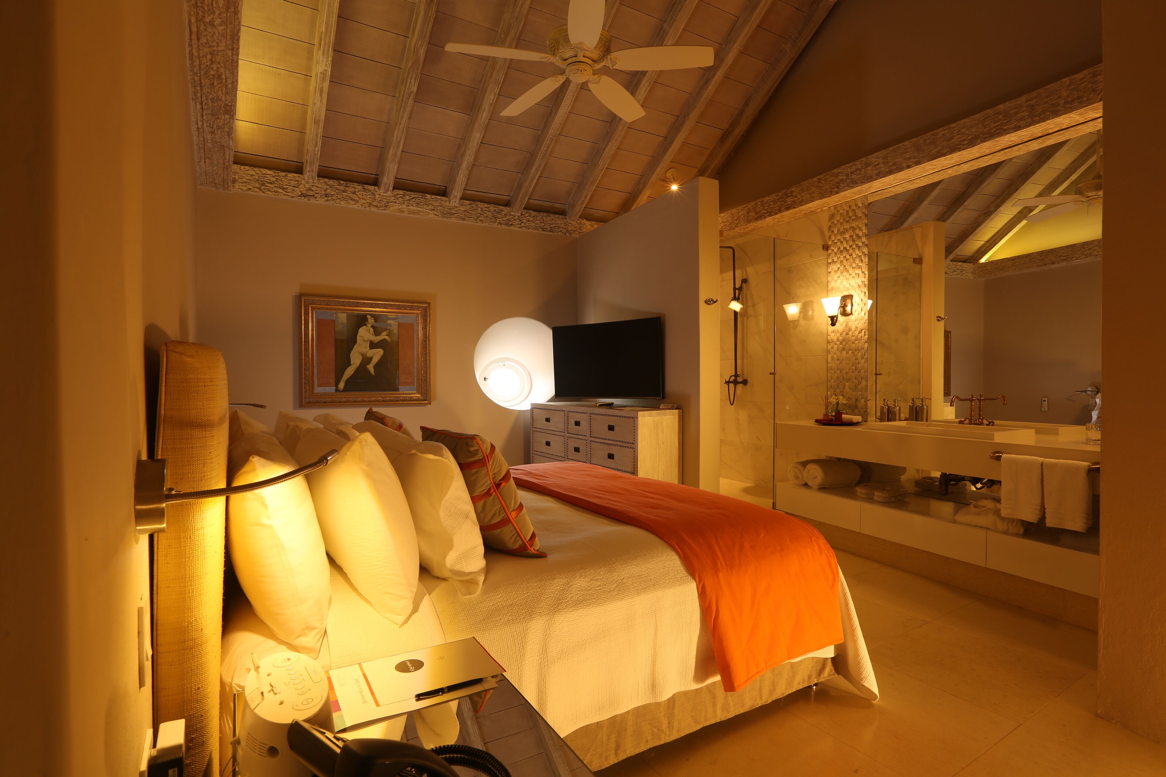 Une chambre à coucher comprenant un lit, une table de chevet, une lampe, une télévision et un grand miroir.