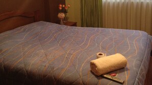 A hotel room with a large bed, a nightstand with a vase of flowers, and a window with curtains.