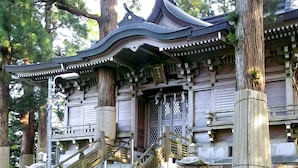 Um edifício tradicional japonês com telhado curvo, pilares de madeira e uma escadaria de pedra que leva à entrada.