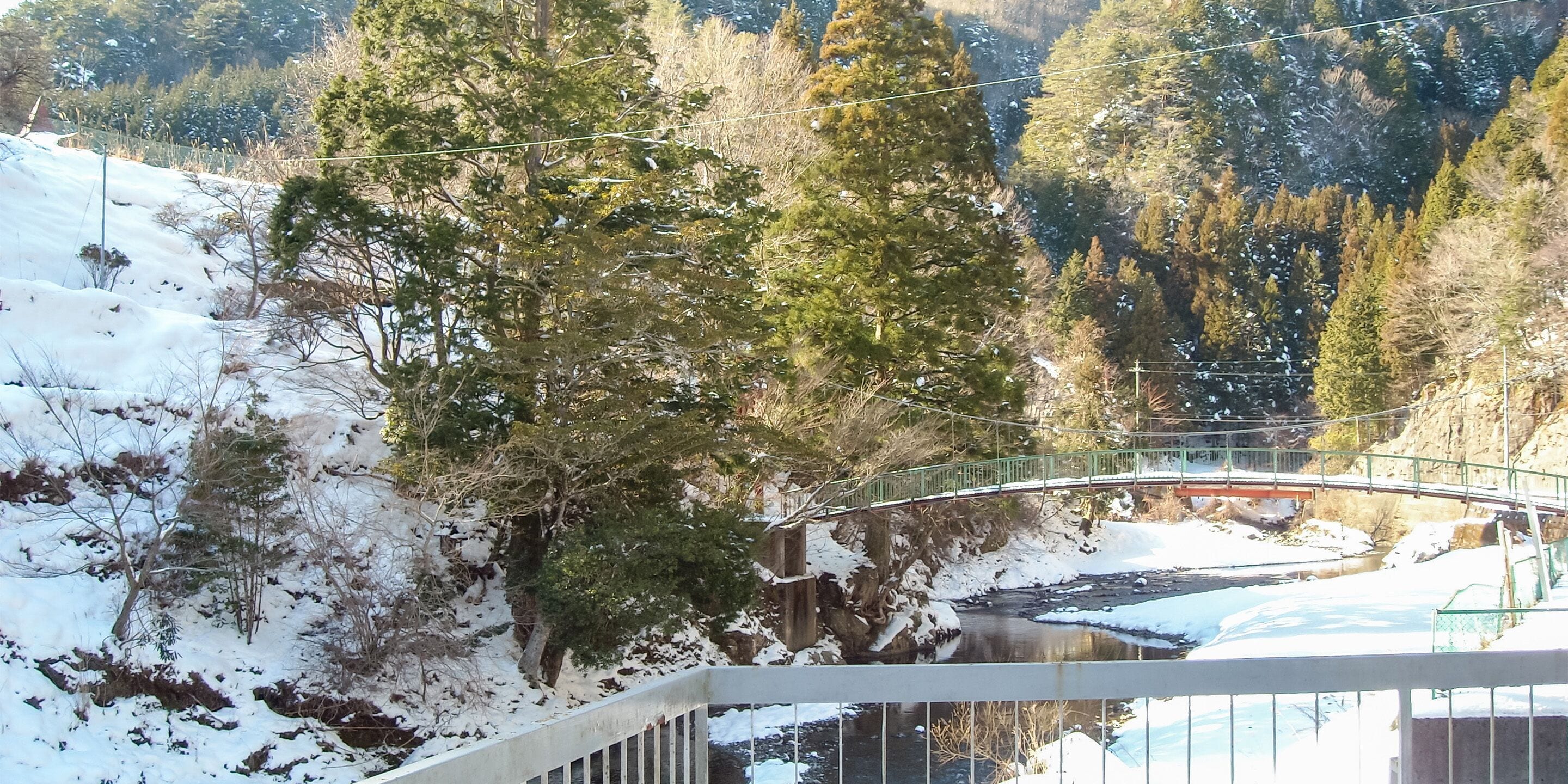 A snow-covered landscape with a bridge, trees, and a river.