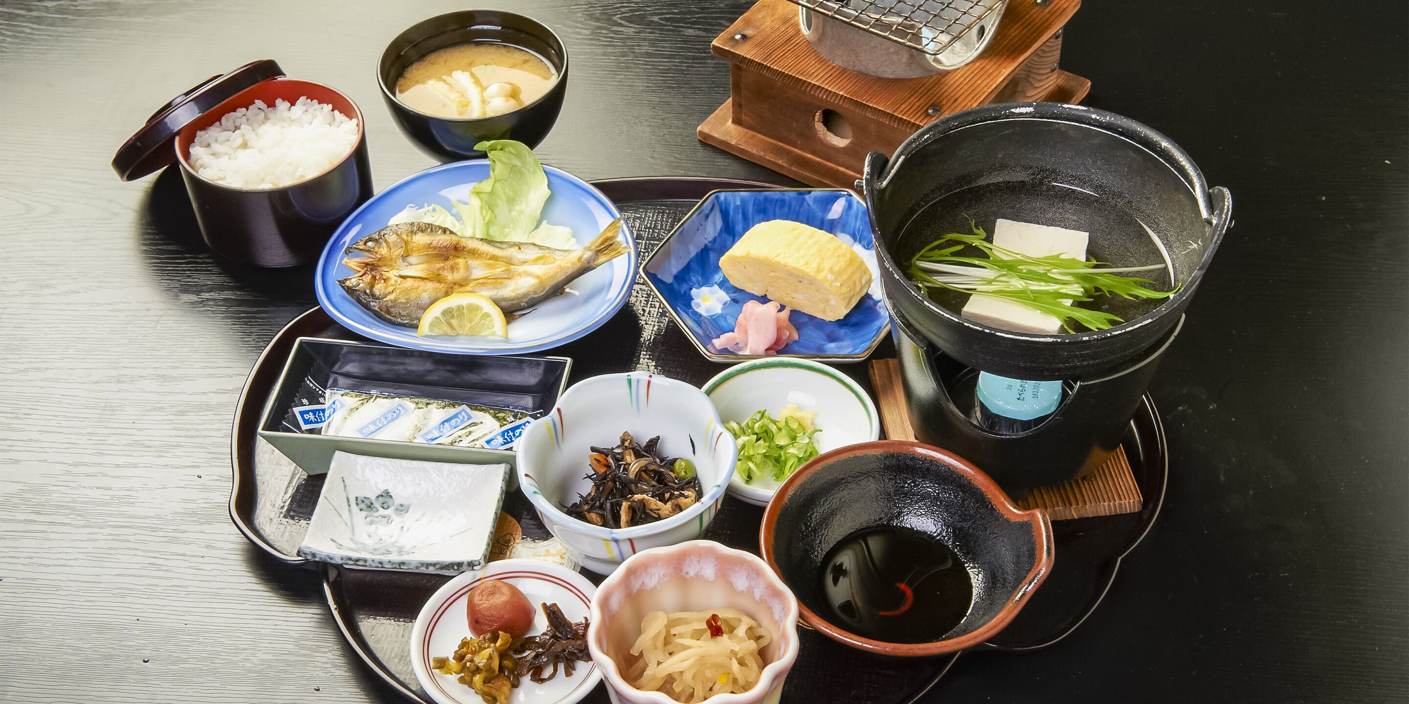 A variety of Japanese dishes including rice, fish, tofu, and pickled vegetables on a tray.