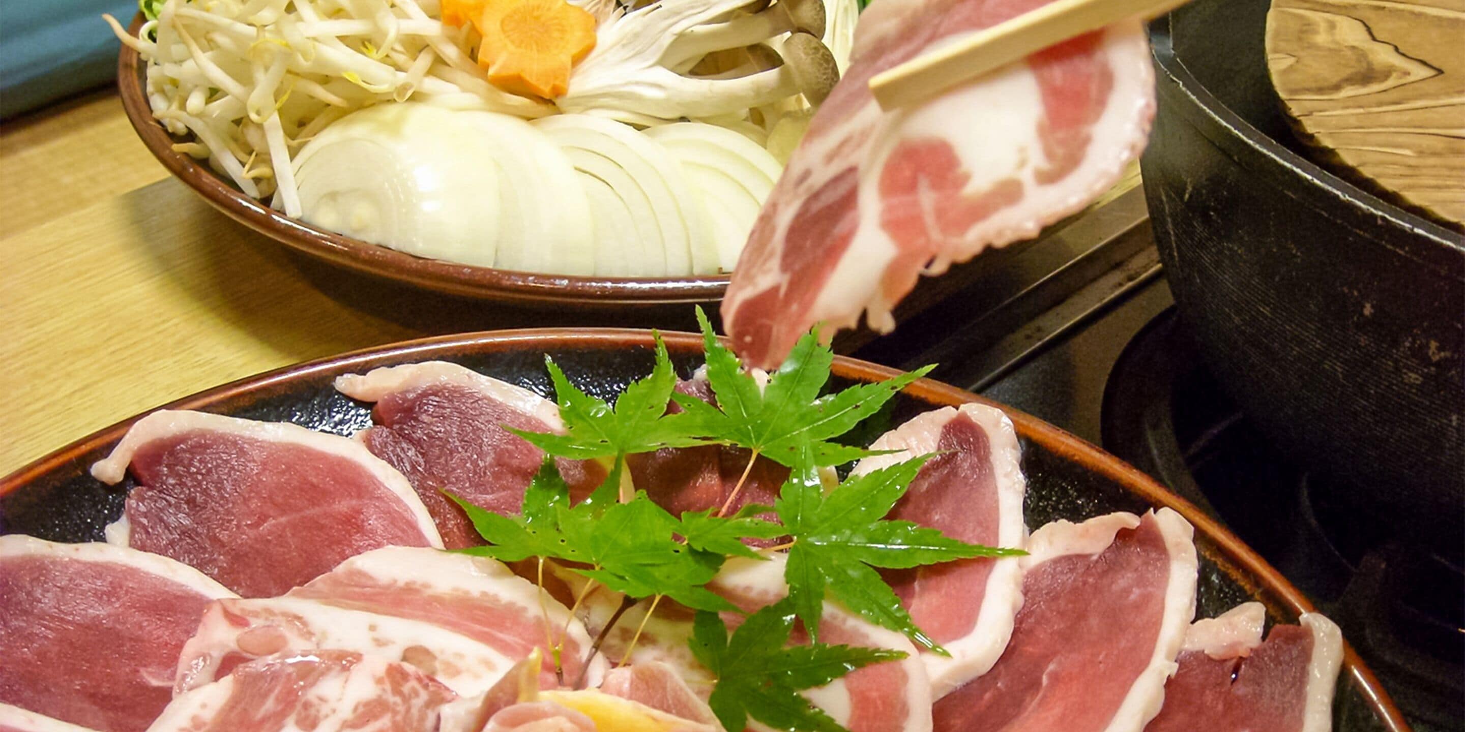 A bowl of sliced meat and vegetables, a plate with meat slices and a green leaf garnish, and a pot on a stove.