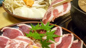 A bowl of sliced meat and vegetables, a plate with meat slices and a green leaf garnish, and a pot on a stove.