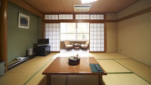 Um quarto japonês tradicional com tatames, uma mesa baixa de tatame, uma televisão e uma janela com biombos shoji.