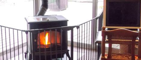 A wood-burning stove with a visible fire, a chair, and a television.