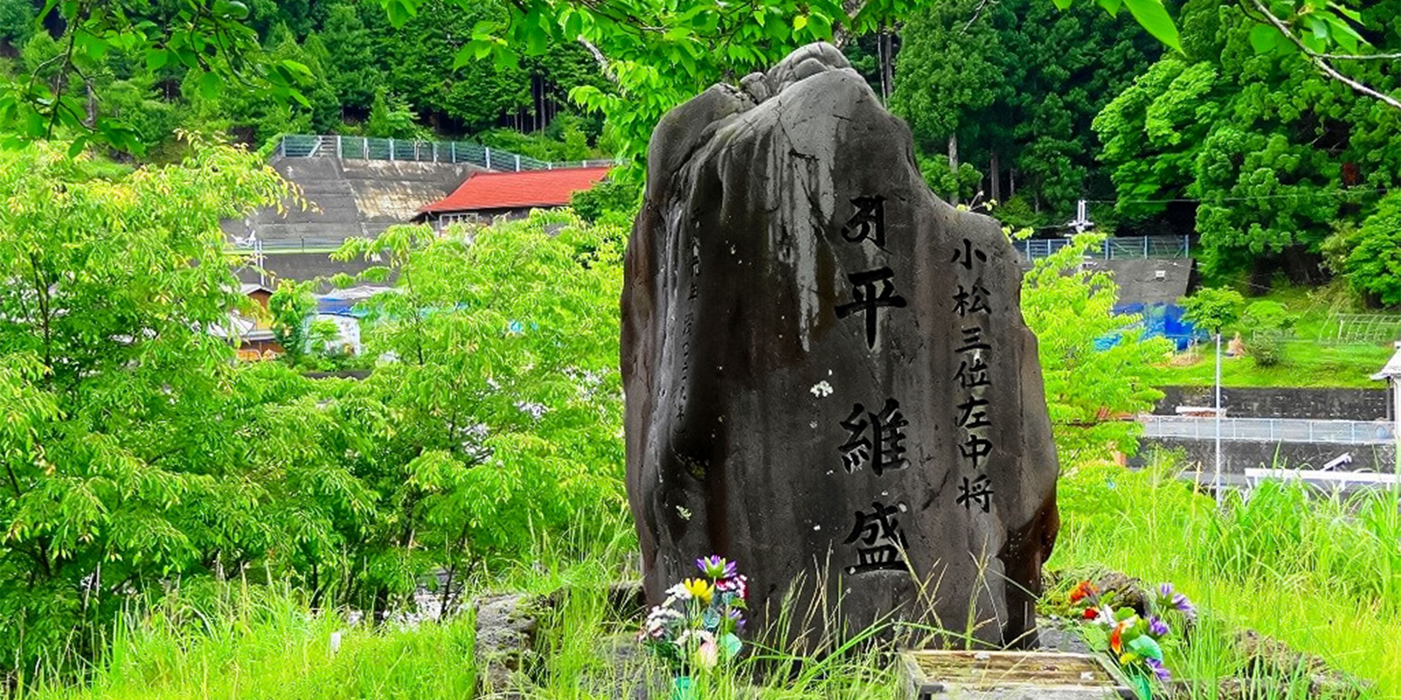 A stone monument with inscriptions, surrounded by lush greenery and a small pond.