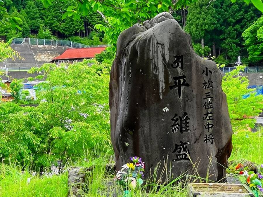 A stone monument with inscriptions, surrounded by lush greenery and a small pond.
