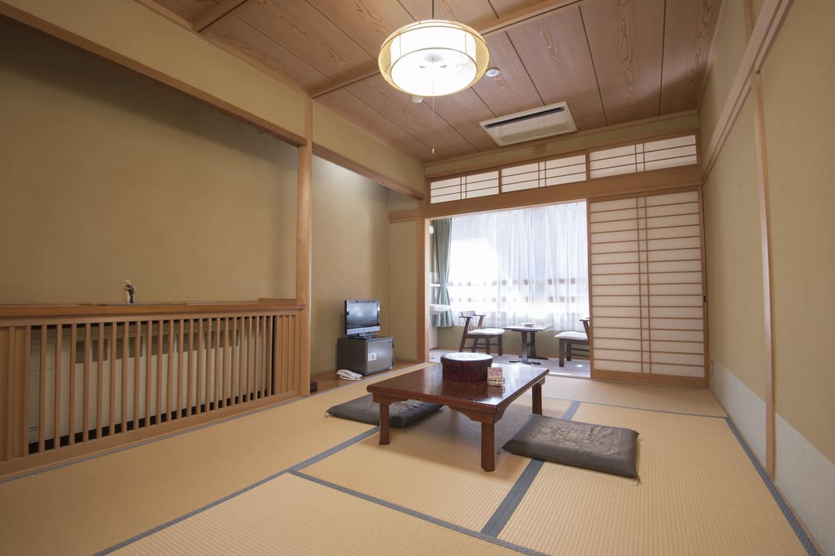 Una habitación tradicional japonesa con suelo de tatami, una mesa baja, cojines, un televisor y puertas correderas.