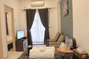 A hotel room with a bed, a desk with a computer, a chair, a coffee maker, and a window with curtains.
